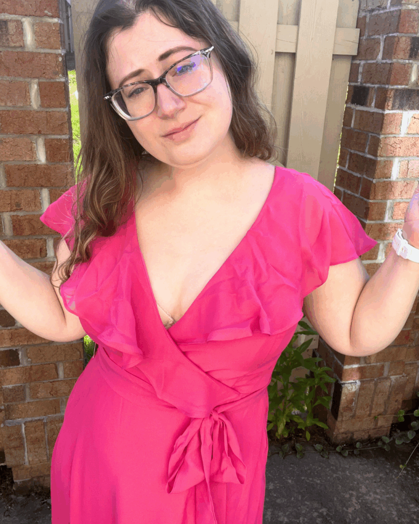 Woman in a hot pink Birdy Grey Jackson chiffon bridesmaid dress with flutter sleeves, shrugging playfully while posing outdoors.