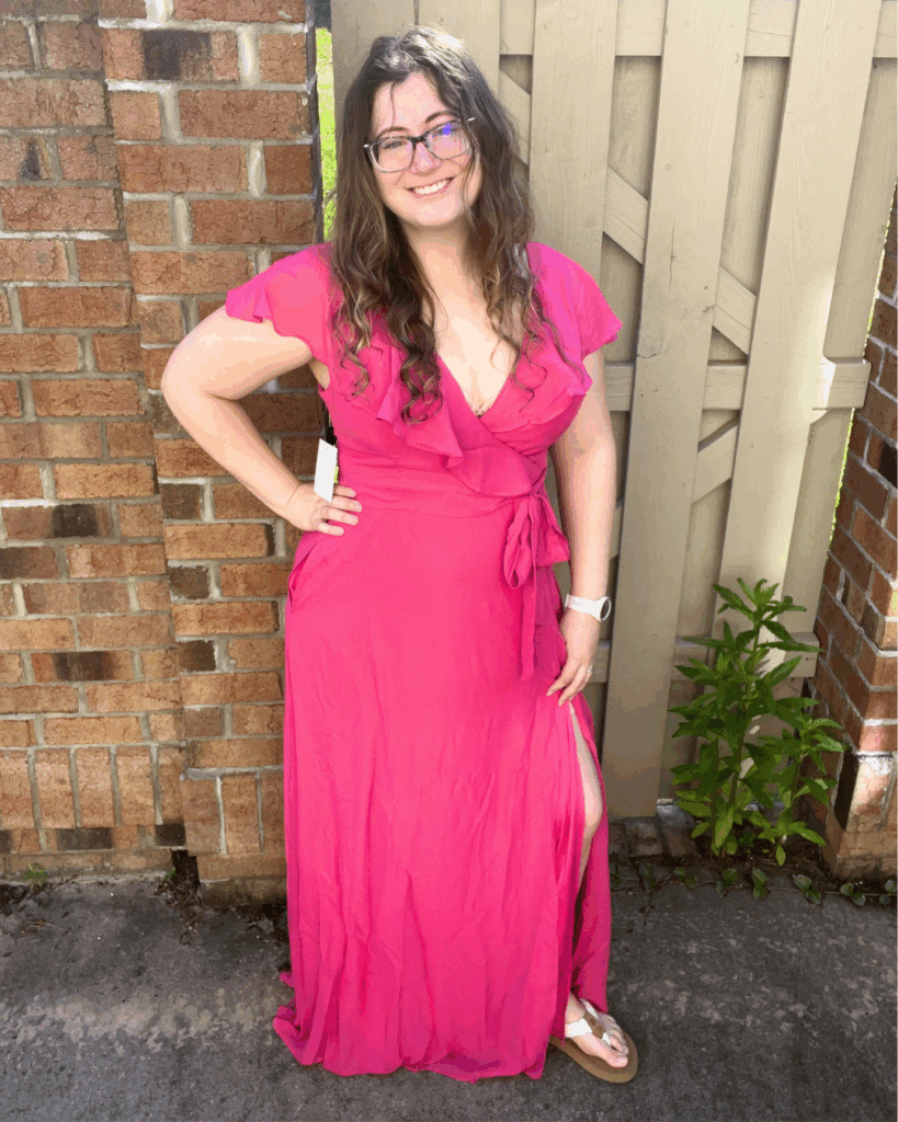 Woman smiling and posing with hand on hip in a hot pink, Barbie pink Birdy Grey Jackson chiffon bridesmaid dress with leg slit, styled with white sandals.